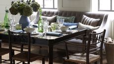 Wood dining table with white crockery, green glassware and a grey banquette