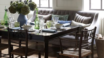 Wood dining table with white crockery, green glassware and a grey banquette