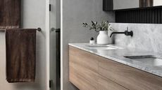 contemporary bathroom with floating timber vanity topped with marble and two brown towels hanging on wall