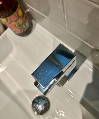 Shiny silver faucet in bathroom with grey tiles and soap