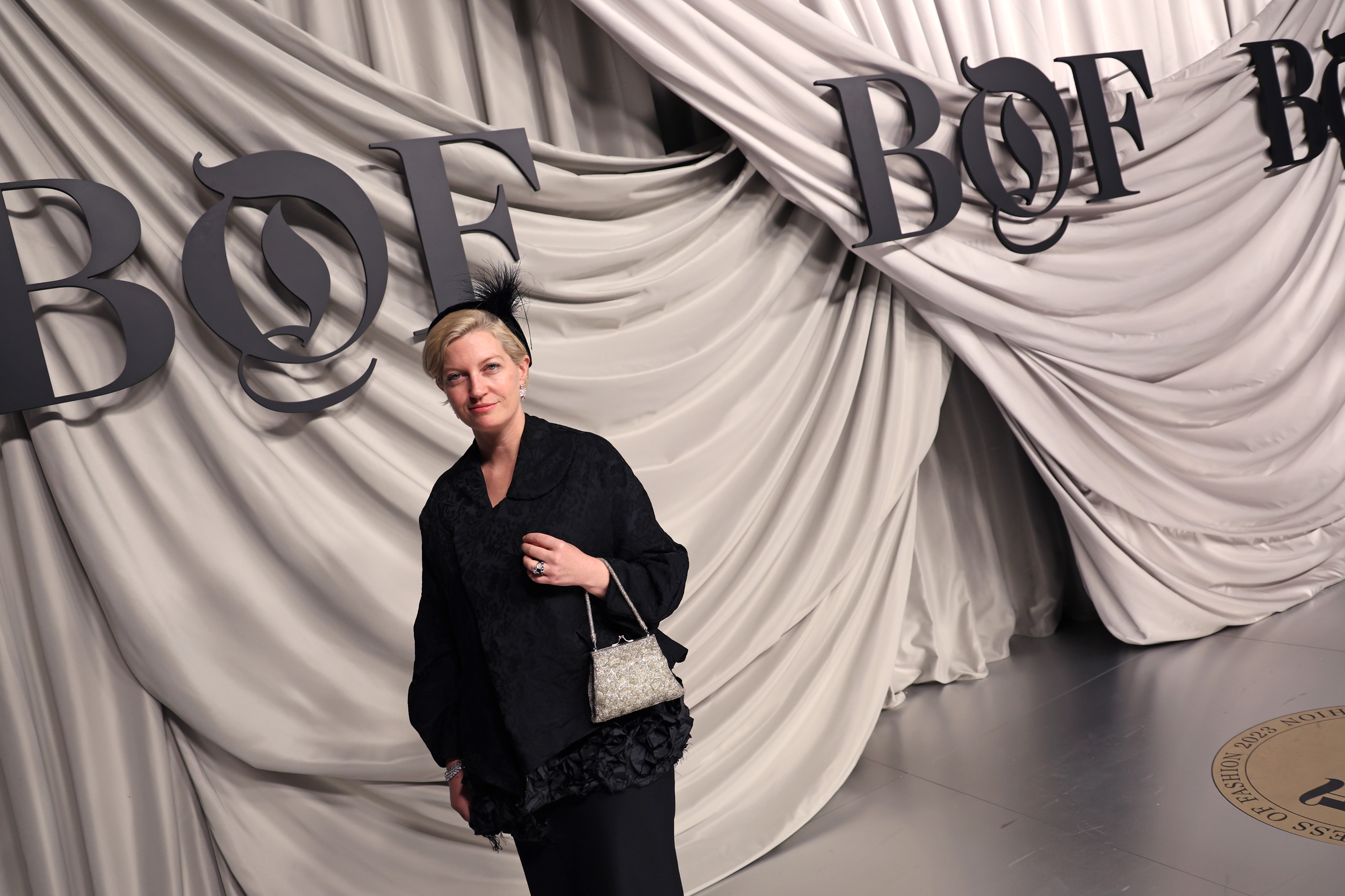 Woman posing in front of decorative draping and the Business of Fashion logo wearing a black feather headband and black outfit