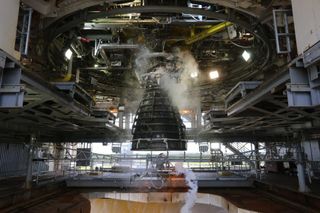 A large engine hangs in the center of a room, shrouded in smoke.