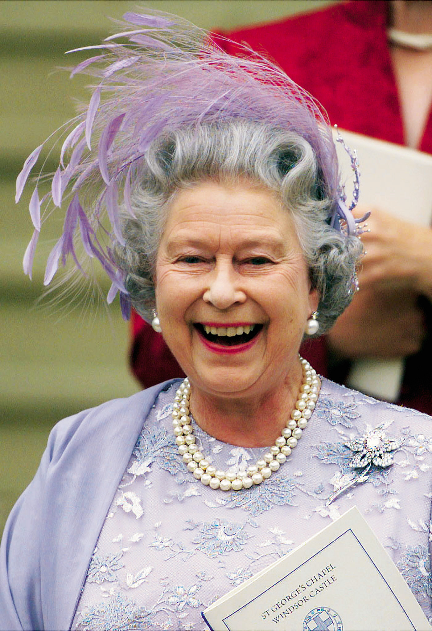Queen Elizabeth wearing a lilac feathered hat and matching dress and smiling at Prince Edward's wedding