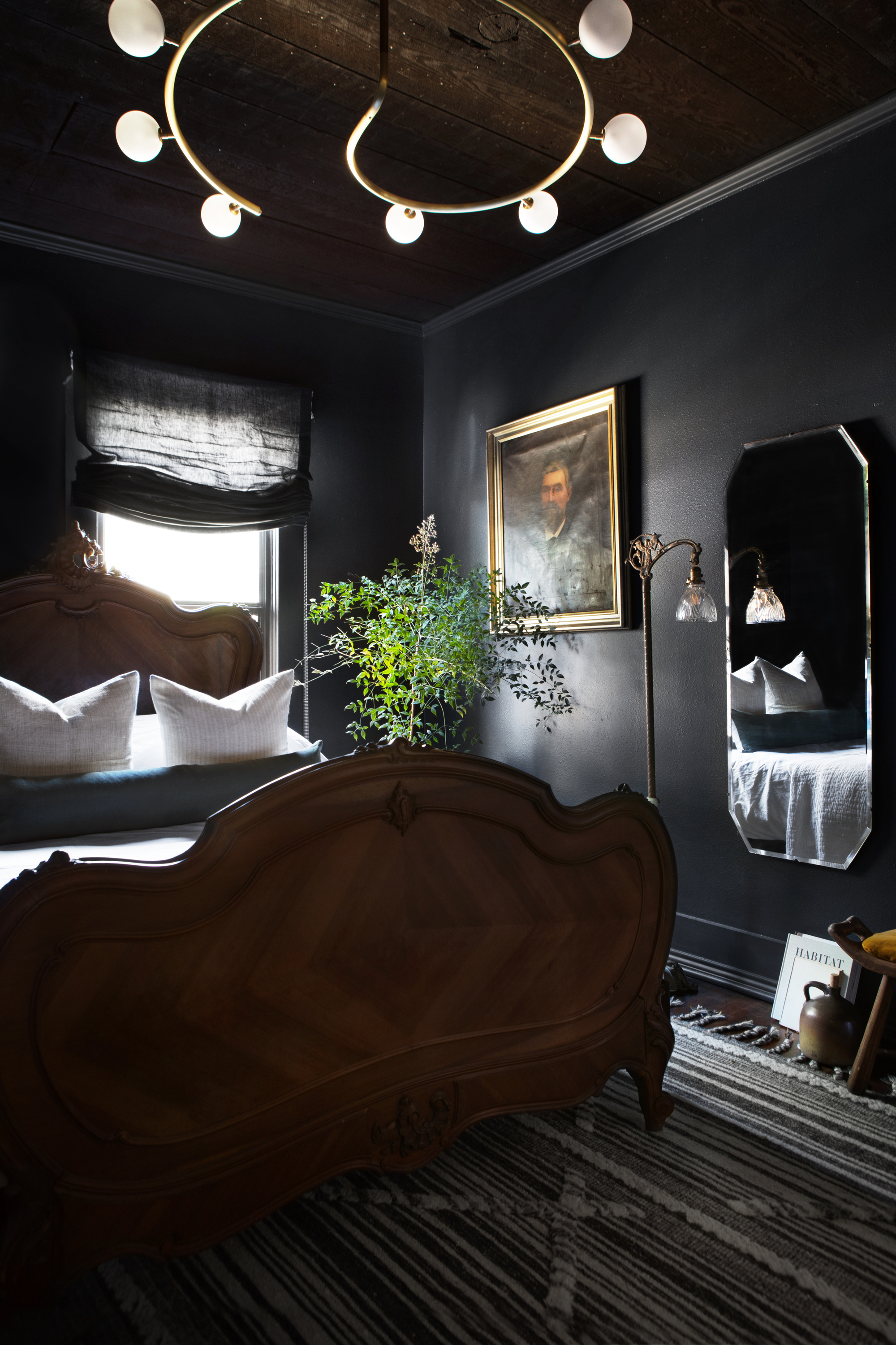 A bedroom with dark charcoal toned walls and a large, gothic style bed