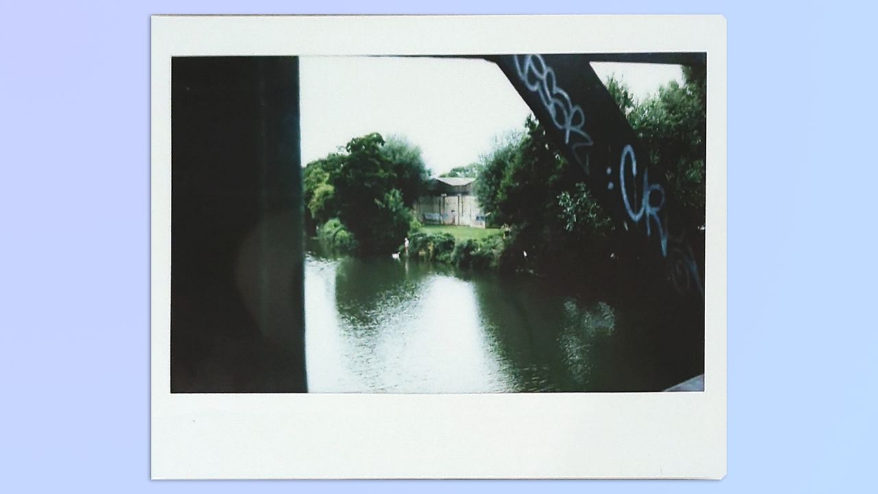 A photo of a river and trees in the distance framed by a bridge, taken on a Fujifilm Instax Wide 400 instant camera