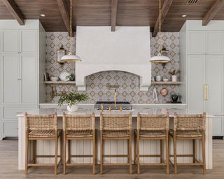 Kitchen with island and bar stools, range, neutral cabinets and patterned backsplash