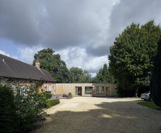 stone and brick house with timber clad side extension and gravel driveway