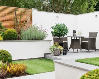 White rendered raised beds in a walled garden with square patio area and bistro table and chairs.