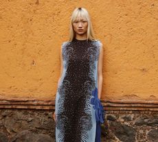 Woman wearing brown and blue Farfetch dress leaning on orange wall