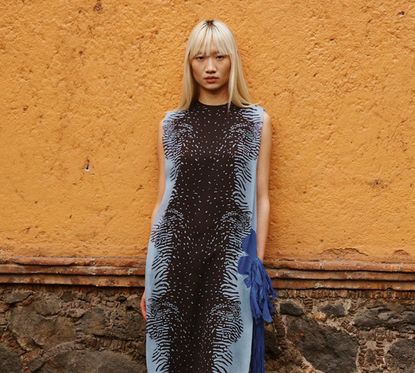 Woman wearing brown and blue Farfetch dress leaning on orange wall