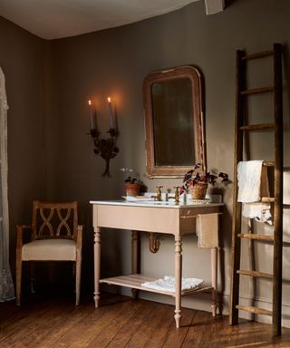 pink wooden washstand in bathroom with dark green walls, towel ladder and wooden flooring