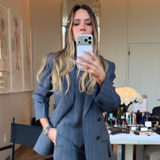 Victoria Beckham takes a mirror selfie wearing s dark grey three-piece suit with grey pointed-toe heels.