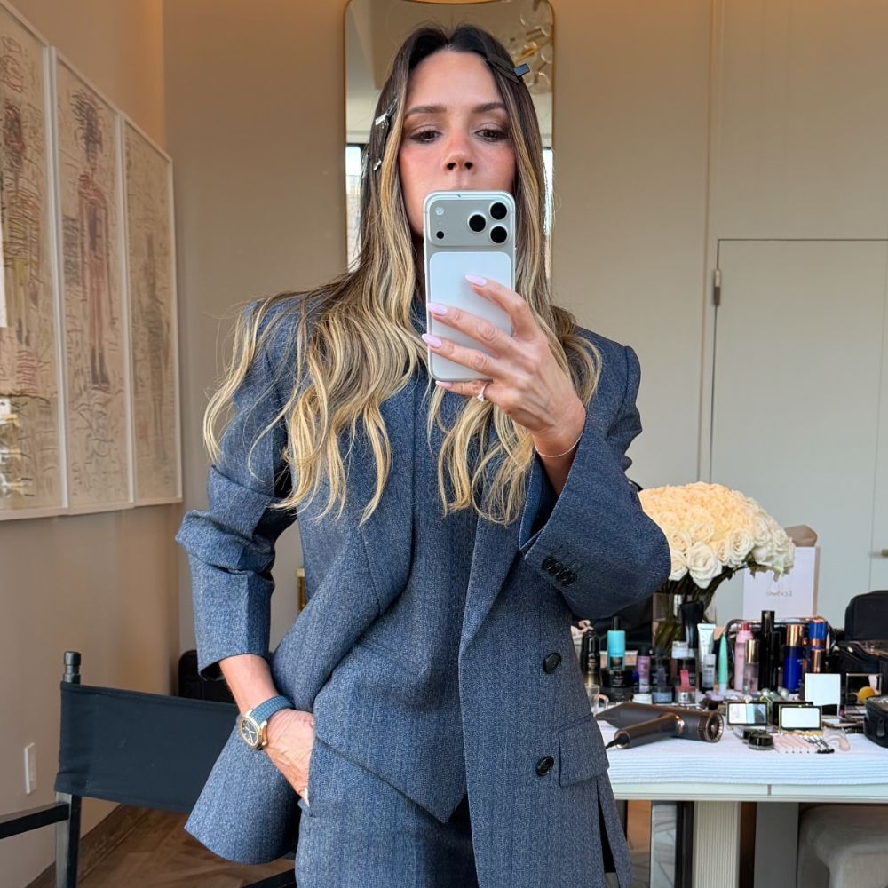 Victoria Beckham takes a mirror selfie wearing s dark grey three-piece suit with grey pointed-toe heels.