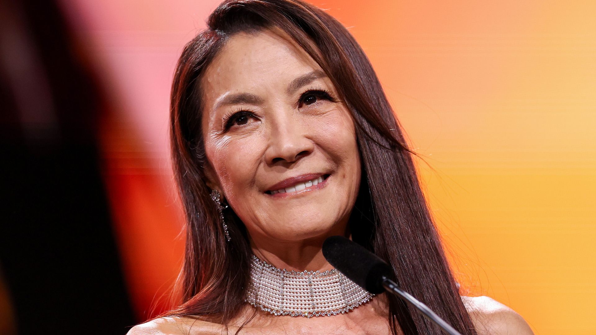 Michelle Yeoh pictured at an awards ceremony with damson brunette hair and a necklace