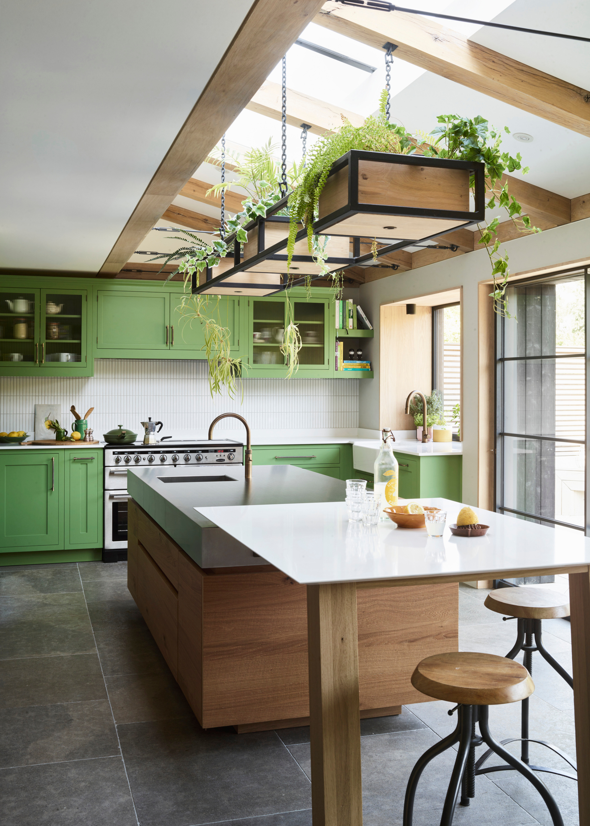 A pastel green and wood kitchen with a multi-level wood and stone island sitting beneath a long hanging planter