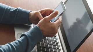 A man using 2FA on his smartphone to access a service on his laptop