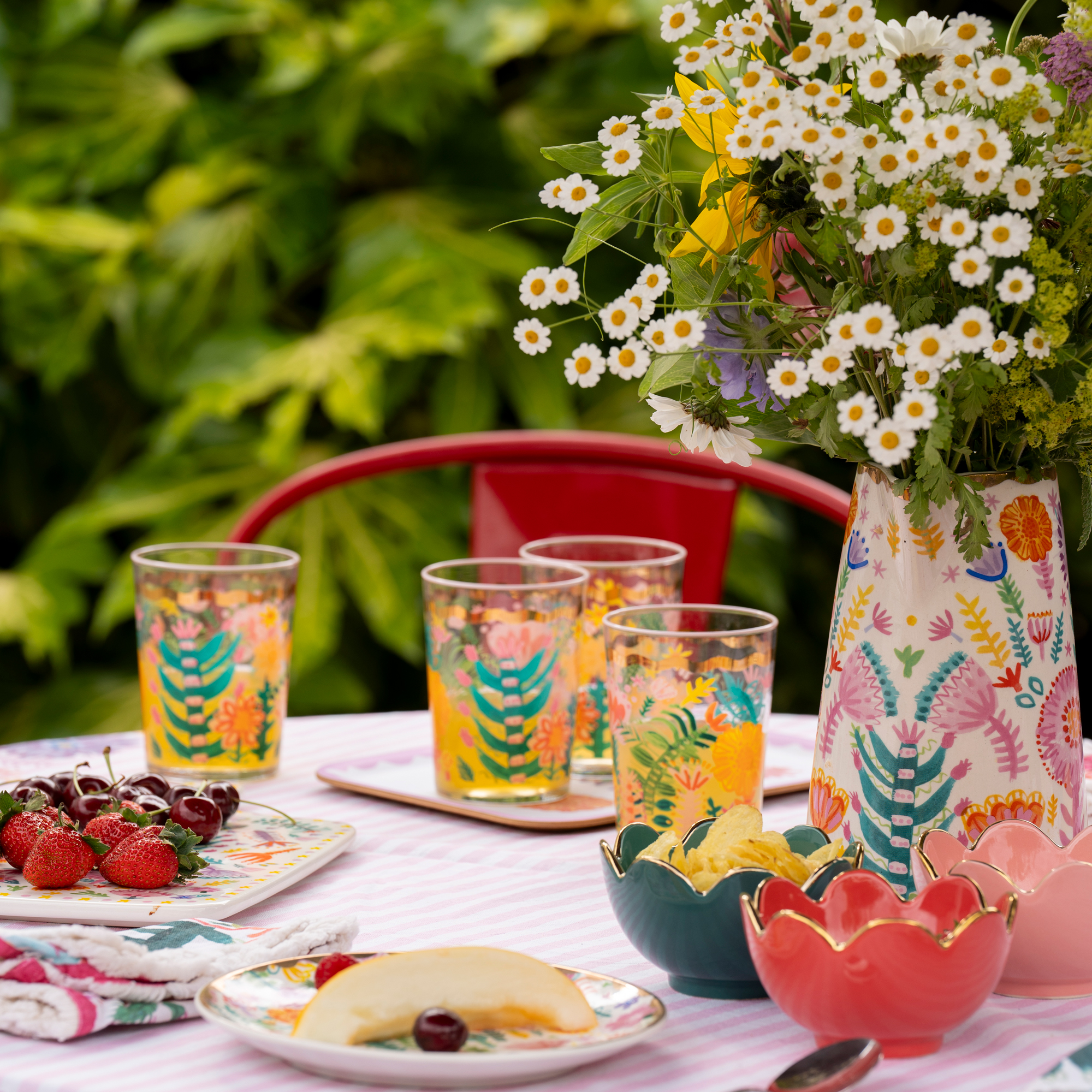 close up of a dining table with painted glasses and candy stripe tablecloth and a jug full of flowers