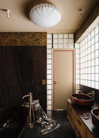 a dark bathroom with a black tub and wooden walls with a glass block wall behind the sinks