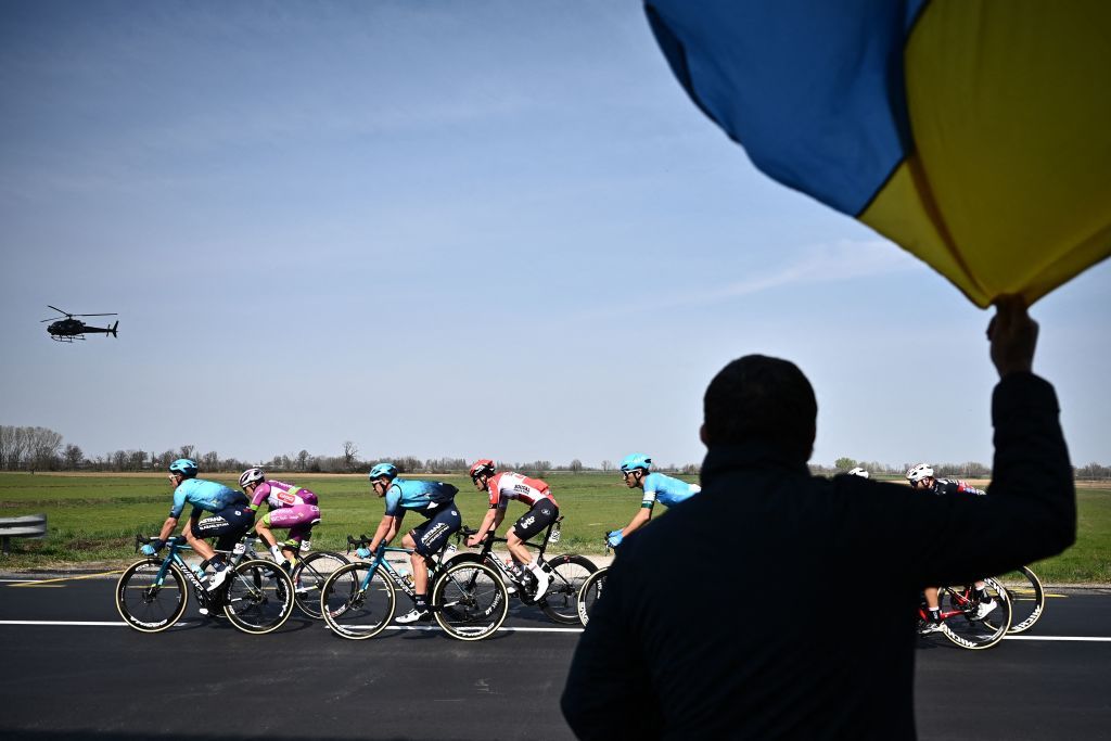 A spectator waves the national flag of Ukraine as From L Team Astanas Yevgeniy Gidich of Kazakhstan Team Bardianis Alessandro Tonelli of Italy Team Astanas Artem Zakharov of Kazakhstan and Team Lottos Filippo Conca of Italy ride near Casteggio south of Pavia Lombardy during the 113th MilanSan Remo oneday classic cycling race on March 19 2022 between Milan and San Remo northern Italy Photo by Marco BERTORELLO AFP Photo by MARCO BERTORELLOAFP via Getty Images