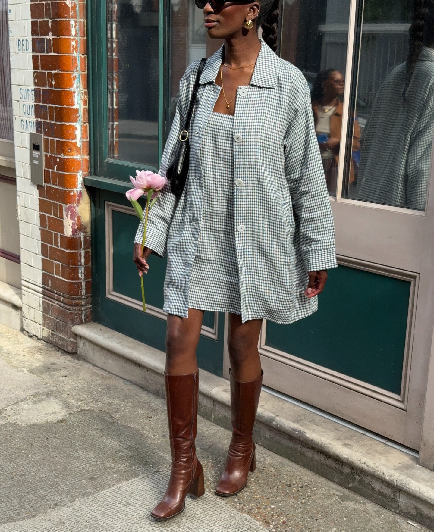 Fashion person Liv Madalline wears a brown shoe outfit. She pairs long from boots with a gingham jacket, matching dress and black shoulder bag. This image was taken from her Instagram recently.