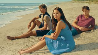 (L to R) Gavin Casalegno as Jeremiah, Lola Tung as Isabel "Belly" Conklin and Christopher Briney as Conrad sit on the beach in The Summer I Turned Pretty season 2 poster art