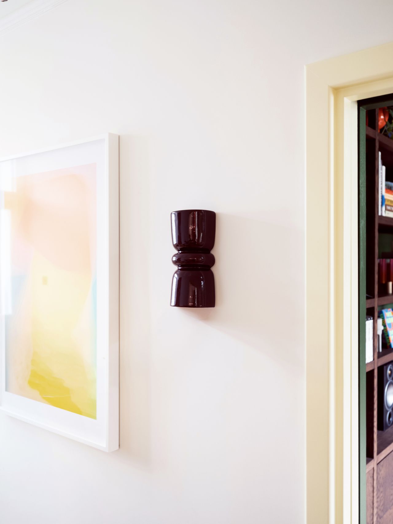 Image of a glossy, sculptural wall sconce in burgundy red on a white wall