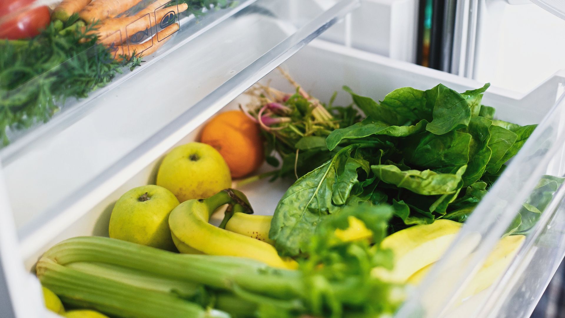 A cripser drawer in a fridge, open to show the fruit and vegetables inside