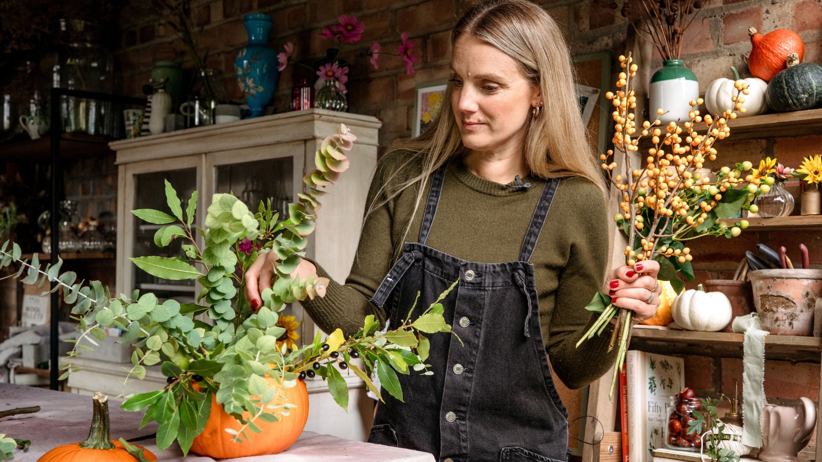 Woman arranging eucalyptus stems into a pumpkin