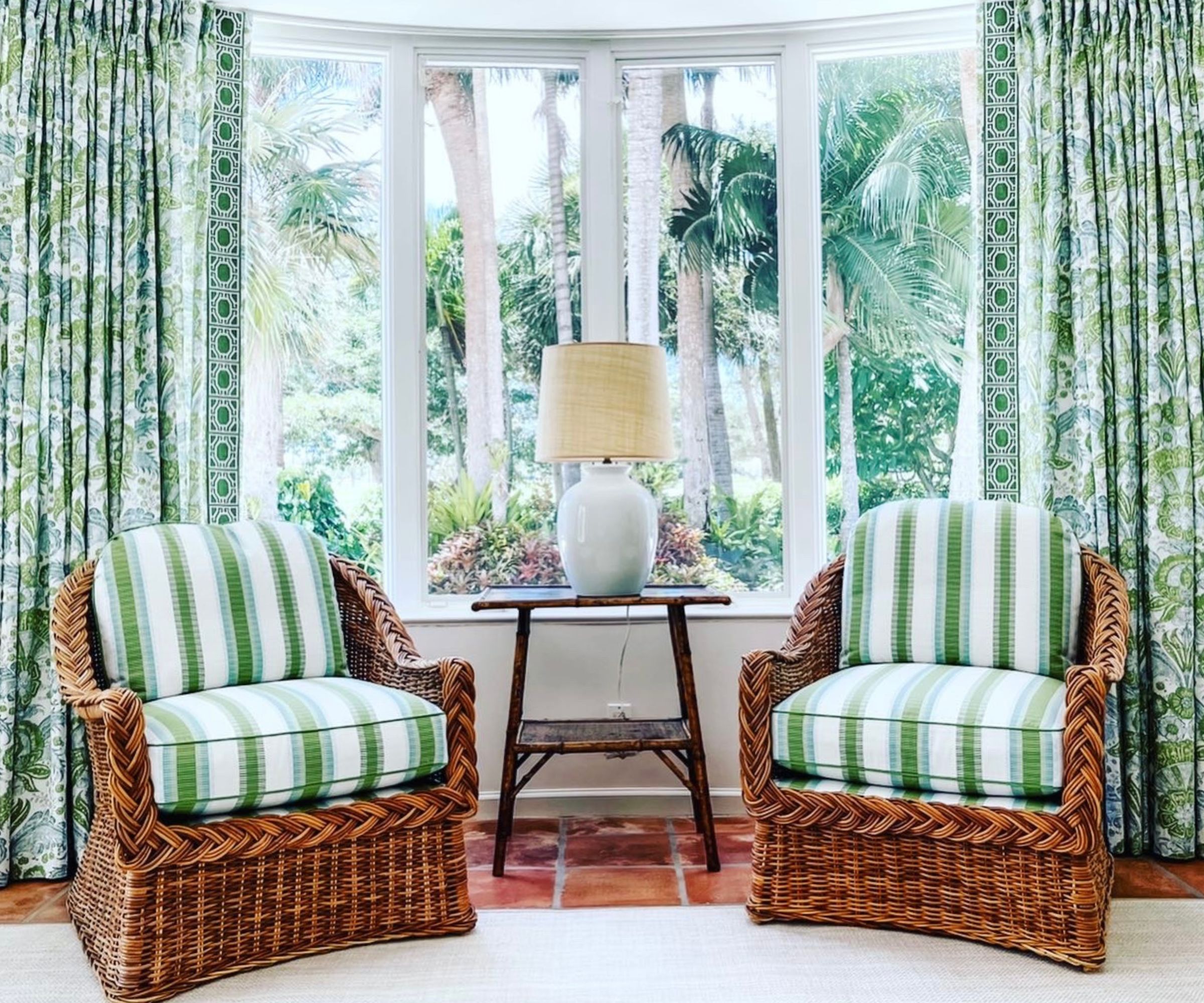 Two antique cane armchairs reupholstered in a green and white fabric, styled in front of a window dressed with green patterned curtains