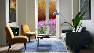 Small grey living room with small sofa and two armchairs positioned with a view to flower garden through French doors