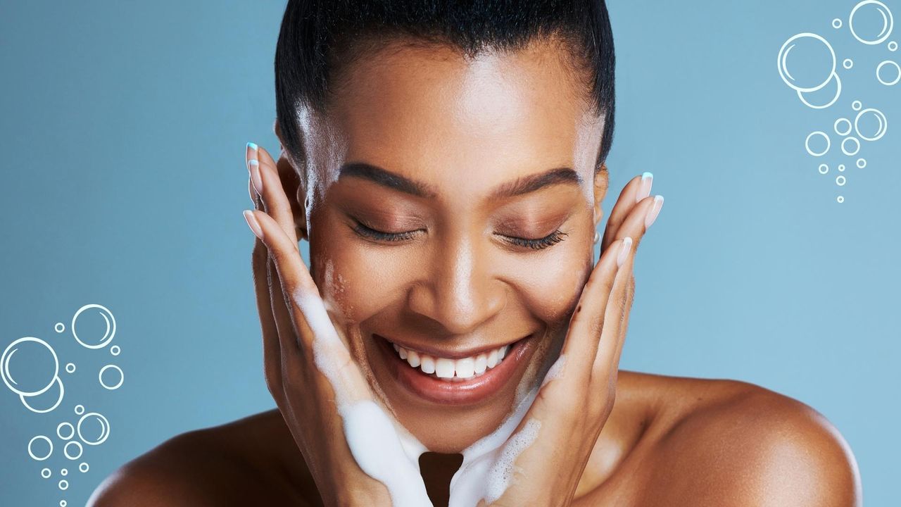 A woman on a blue background washing her face with bubbles, to illustrate how often should you wash your face