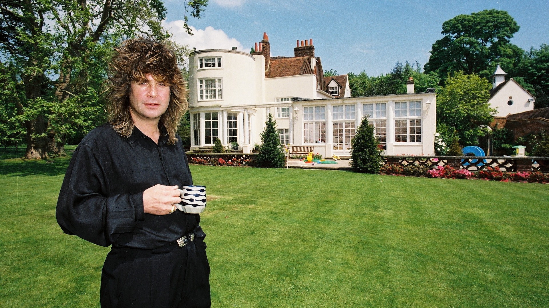 Ozzy Osbourne holding a cup of tea in the garden of his home, May 1988