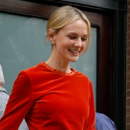 Carey Mulligan wears a persimmon colored top and skirt.