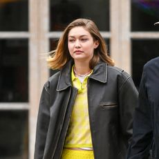 Gigi Hadid wearing a leather jacket and yellow top and walking with Bradley Cooper