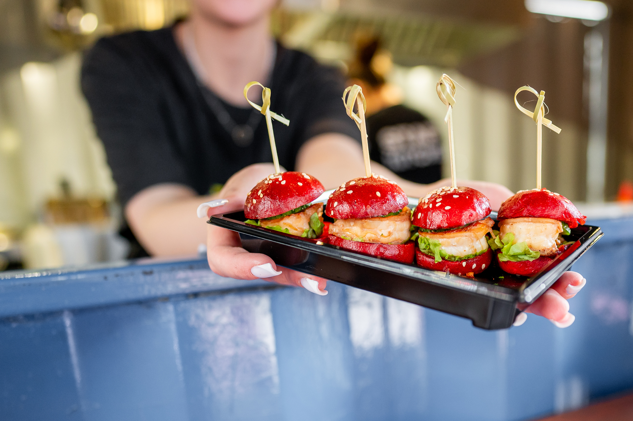 Shrinkflation concept as a person holds a tray with mini burgers 