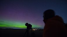 A photo of a stargazer looking up at a night sky full of auroras