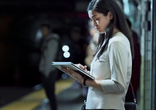 A woman standing on a train platform whilst using a HP tablet.