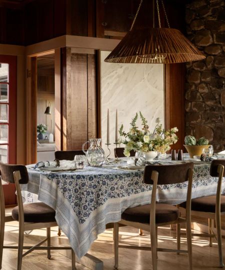 a dining room in shades of blue and brown, a large brown pendant light, a blue tablecloth, and brown chairs