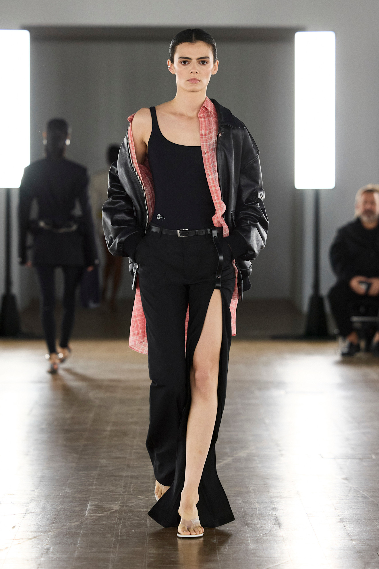 a model at Coperni Spring 2026 wearing a black top, slit pants,a. red and pink flannel, and black leather jacket