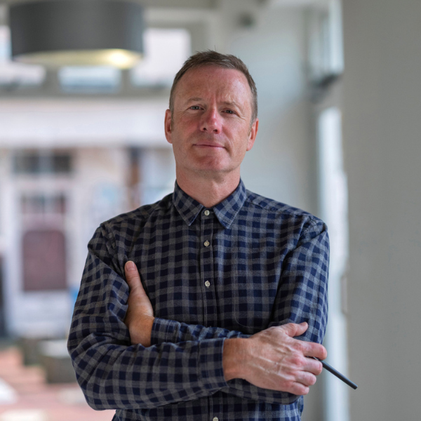 a headshot of nick Duggan, managing director of the radiator centre, with his arms folded looking at the camera with a pen in his hand, wearing a checked blue shirt with short hair