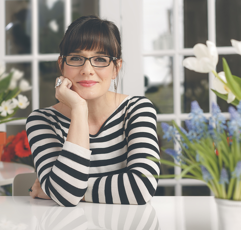 woman in black and white striped top and glasses with flowers in backgorund
