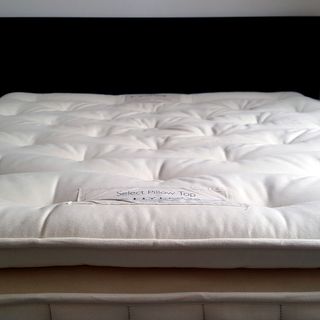 The Hypnos Select Pillow Top mattress being tested in a bedroom with pale pink walls and a black bed
