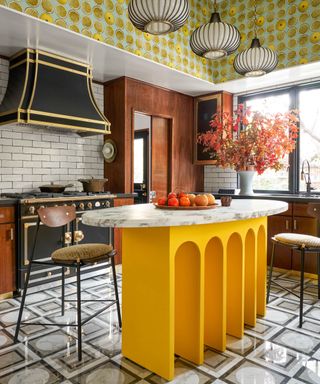 Colorful kitchen with small yellow island with arched base, tiled floor, wood cabinets, wallpaper above window,