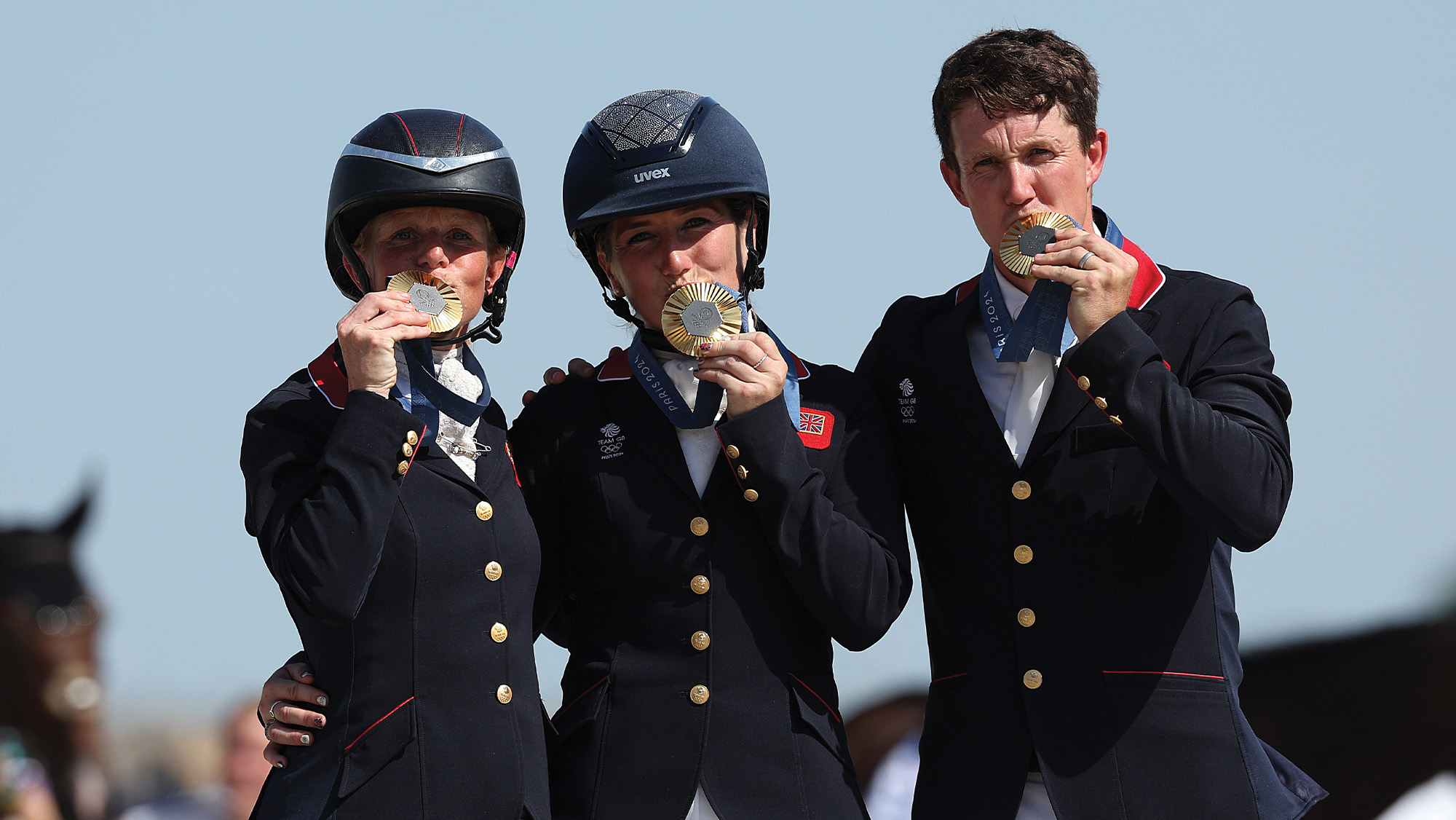 British event riders Ros Canter, Laura Collett and Tom McEwen kiss their gold medals on the podium