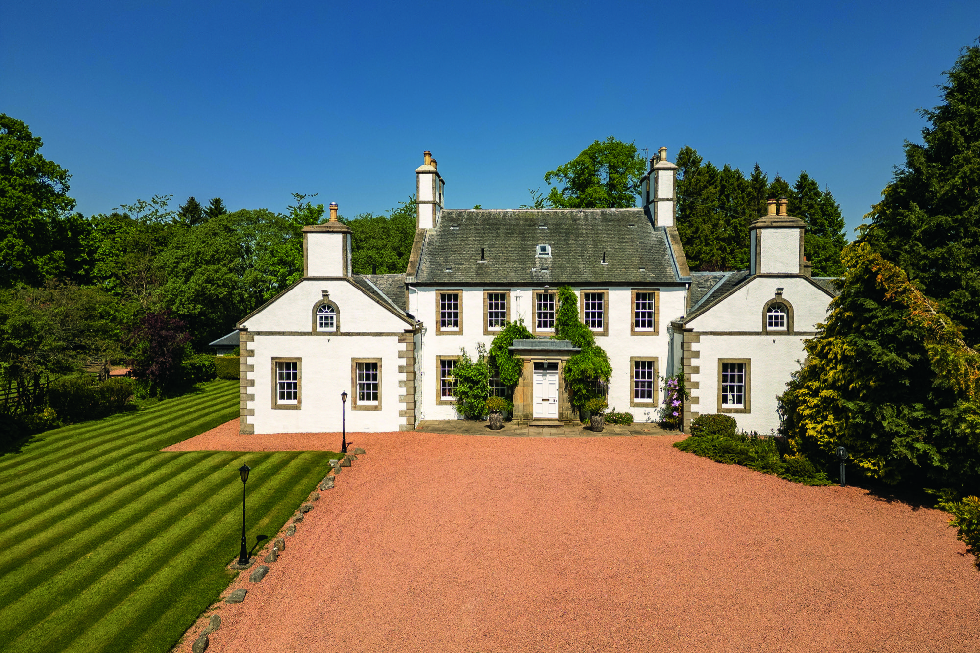 A front view of the generously proportioned Westfield House, surrounded by a gravel drive and painted white with a slate roof