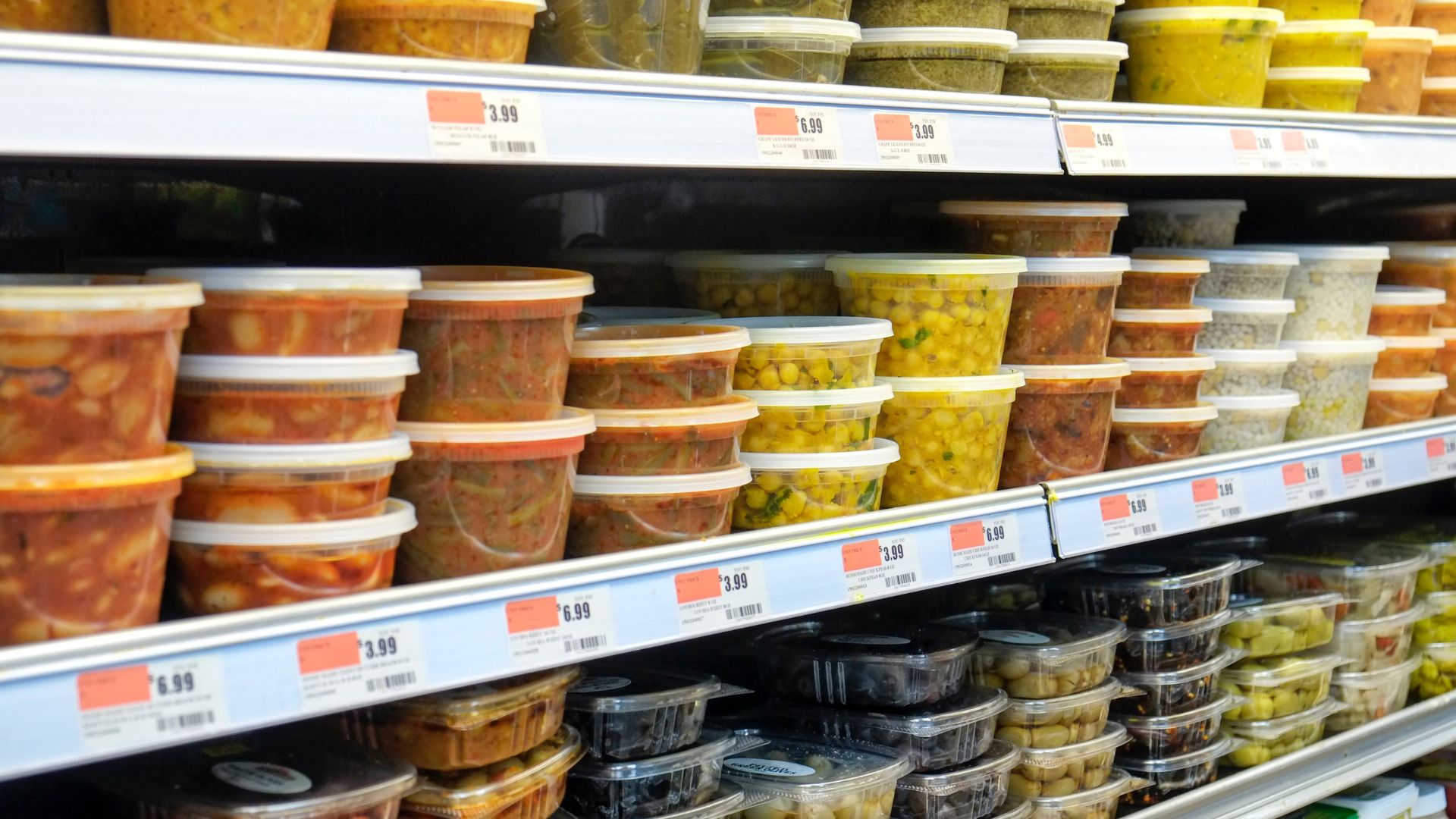 preprepared foods, such as soups, and small packages of olives lined up on shelves in a grocery store