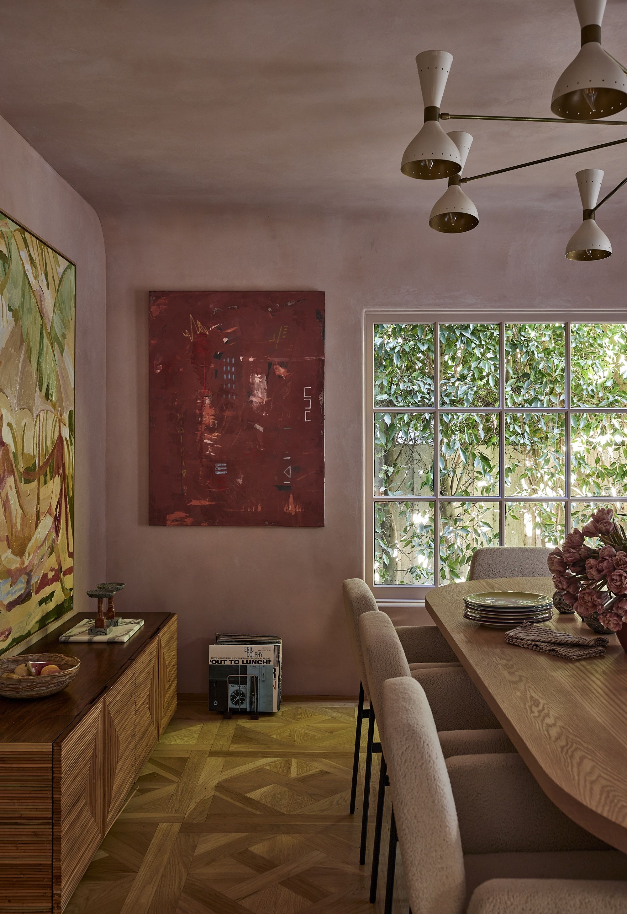a pink dining room with a parquet floor and red artwork and mutli-armed light
