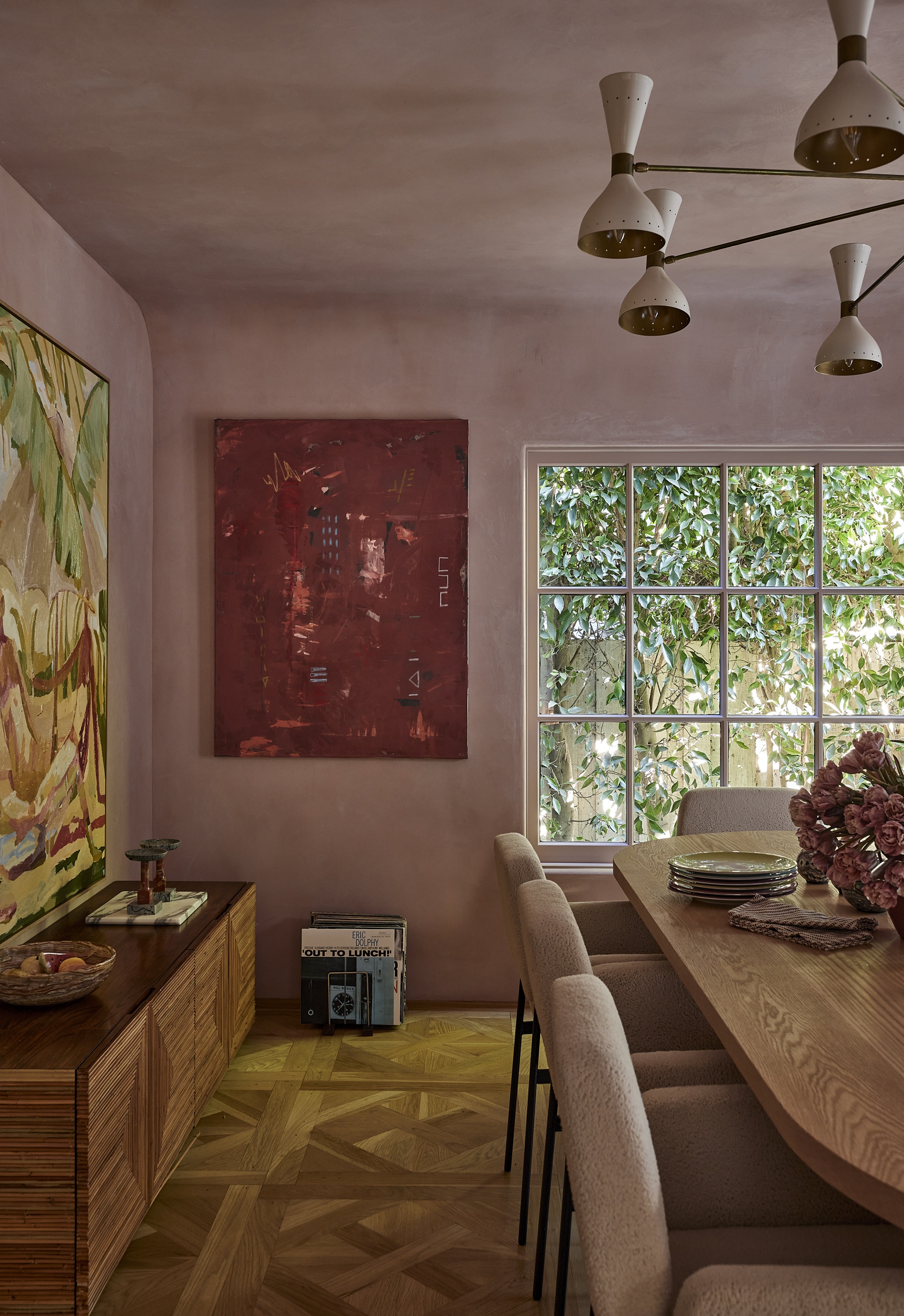 a pink dining room with a parquet floor and red artwork and mutli-armed light