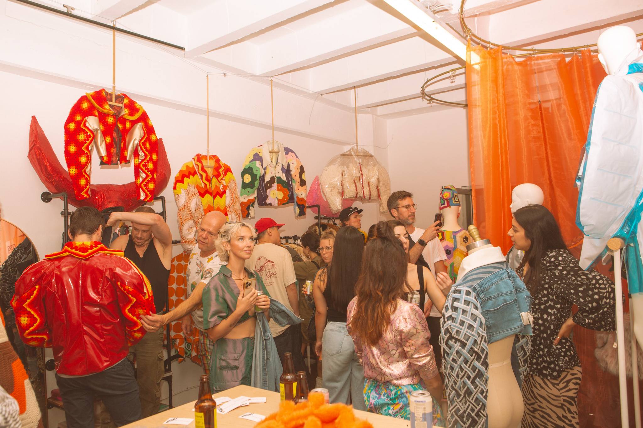 People enjoying a colorful textile exhibition shown alongside a sun-lit picture of a wooden cabin at golden hour.