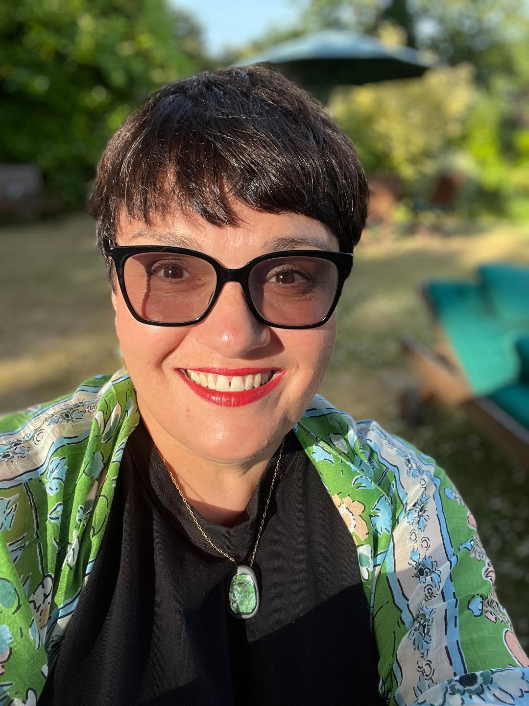 A woman smiling to camera with glasses on and a garden behind her
